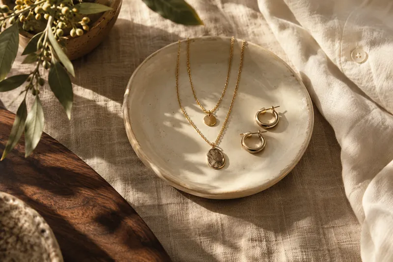 Gold-colored necklaces and hoop earrings on a ceramic dish (AI-generated editorial scene)